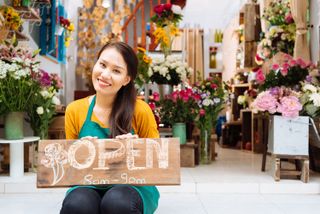 smiling woman holding open sign to shop