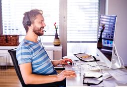 smiling man with headset sitting in front of desktop computer